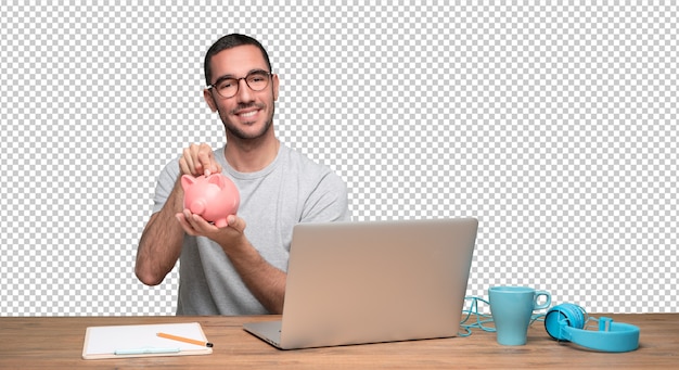 Feliz jovem sentado em sua mesa e segurando um cofrinho