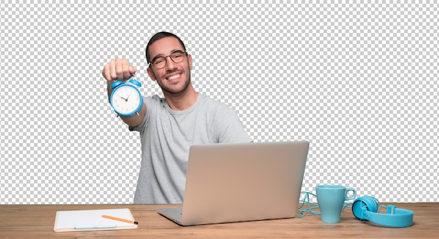 PSD feliz jovem sentado em sua mesa e segurando um despertador