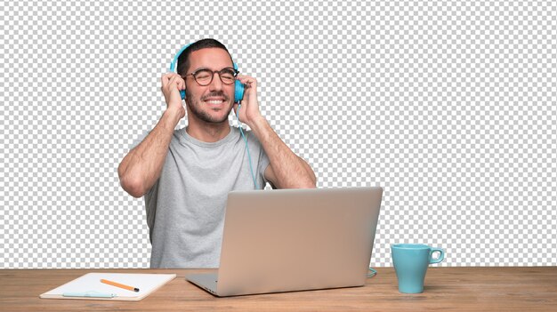 PSD feliz jovem sentado em sua mesa e usando um fone de ouvido