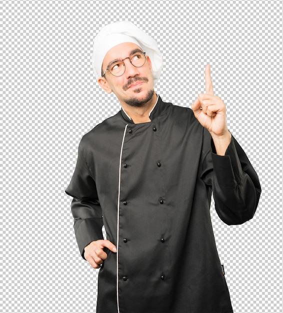 Feliz joven chef apuntando hacia arriba con su dedo