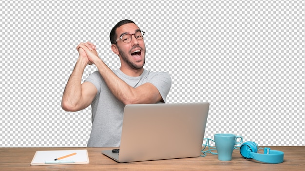 Feliz joven sentado en su escritorio con un gesto de ganador