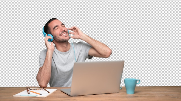 Feliz joven sentado en su escritorio y usando auriculares