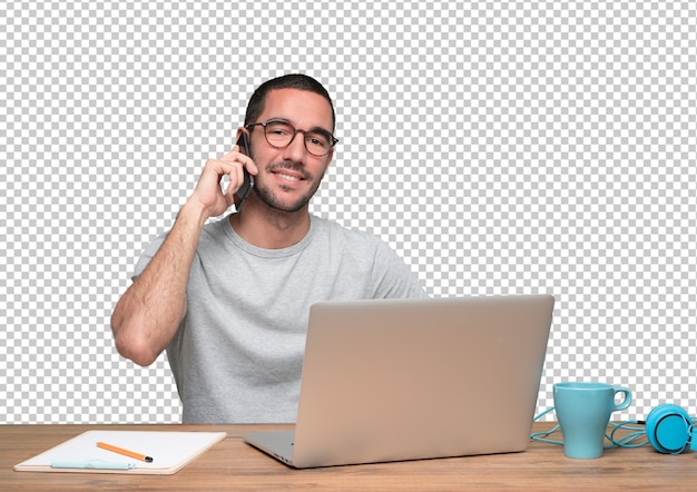 Feliz joven en el teléfono y sentado en su escritorio