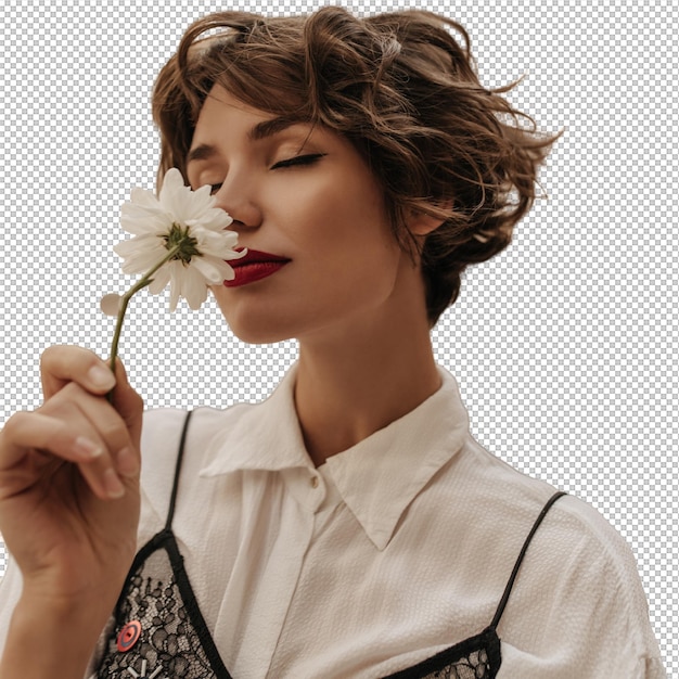 Une femme aux cheveux ondulés en chemise claire avec de la dentelle noire renifle des fleurs en ville Une femme tendre aux lèvres rouges et aux cheveux courts pose dans la rue