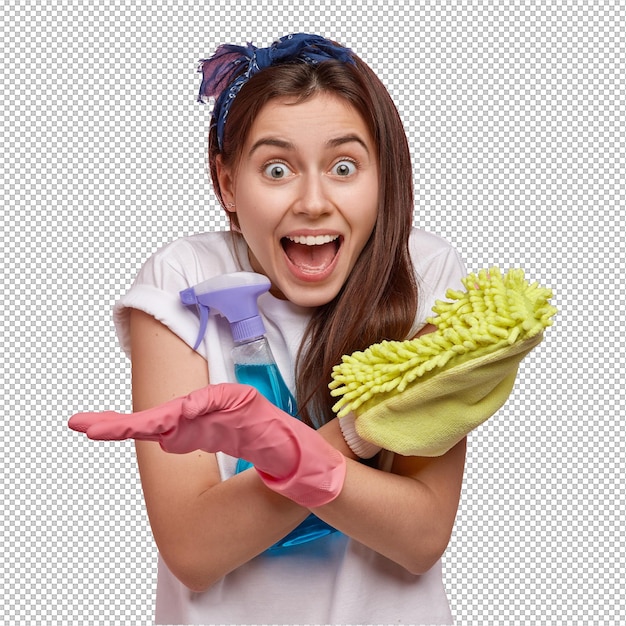 Une femme émotionnelle heureuse croise les mains, tient un balai et un spray de nettoyage, porte un t-shirt blanc et des gants, heureuse de terminer les tâches ménagères à temps, pas en retard pour le rendez-vous, pose contre un mur rose, bonne humeur pour le nettoyage.