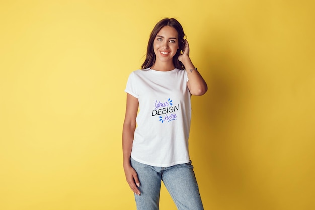 Une femme heureuse en T-shirt blanc et en jeans bleus posant devant un fond jaune