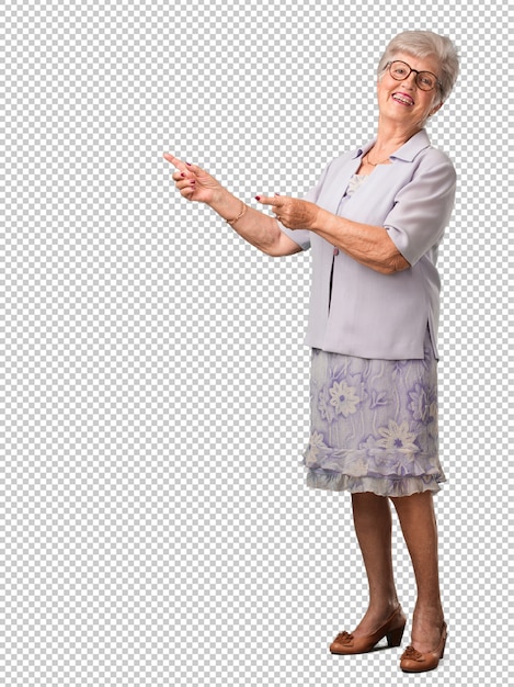 Femme senior complète du corps pointant sur le côté, souriant surpris de présenter quelque chose