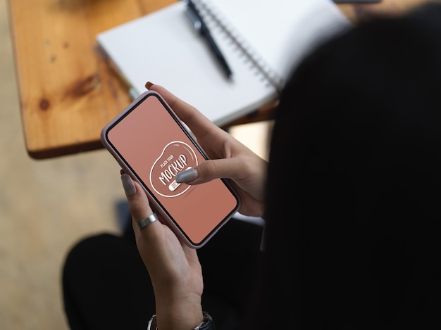 Fotografía cenital de mensajes de texto femeninos en un teléfono inteligente simulado mientras está sentado en la mesa de trabajo