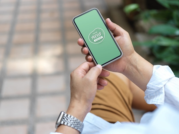 Fotografía recortada de un joven sosteniendo un teléfono inteligente simulado mientras está sentado al aire libre