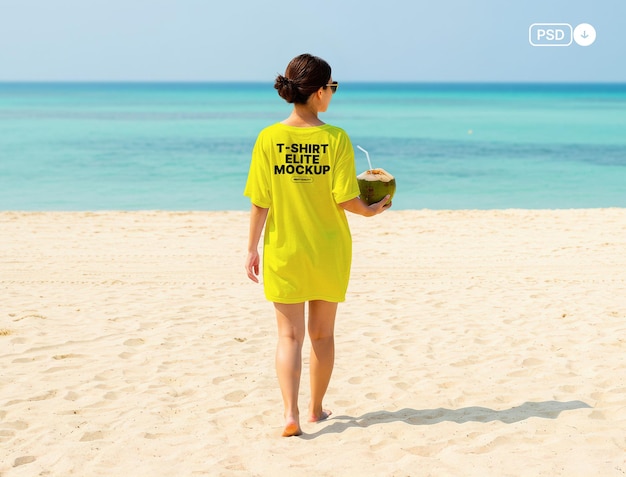 Frau an einem Strand, die ein T-Shirt-Kleid trägt und ein Kokosnussgetränk hält