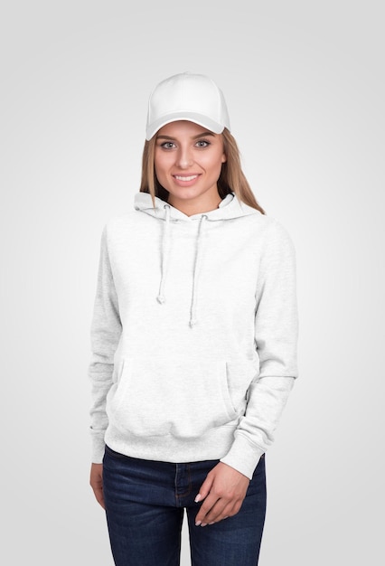 Frau mit weißem Hoodie und Kappe lächelt und posiert vor der Kamera