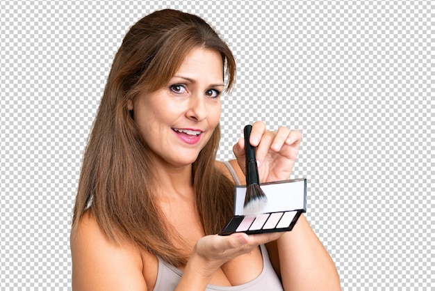 Frau mittleren Alters über isolierten Hintergrund mit Make-up Palette und glücklich