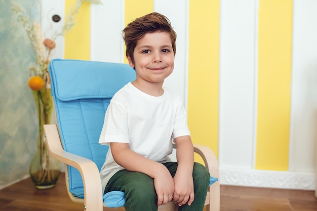 Un garçon heureux assis sur une chaise souriant à la caméra.