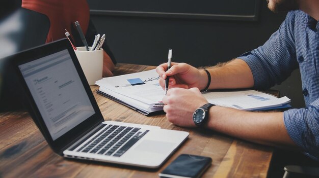 Gente de negocios colaborando en un escritorio de madera revisando documentos y usando una computadora portátil