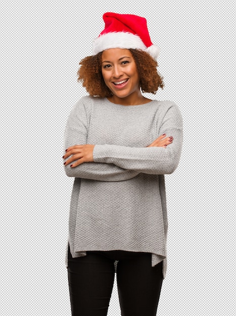 Giovane donna di colore che indossa un cappello da Babbo Natale che attraversa le braccia, sorridente e rilassato