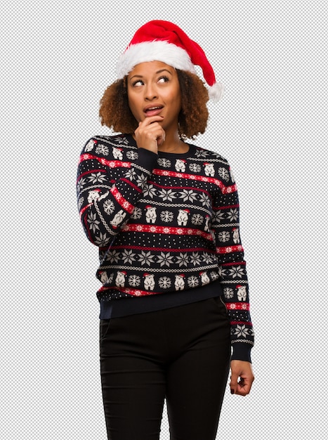 Giovane donna di colore in un maglione di Natale alla moda con stampa dubbioso e confuso