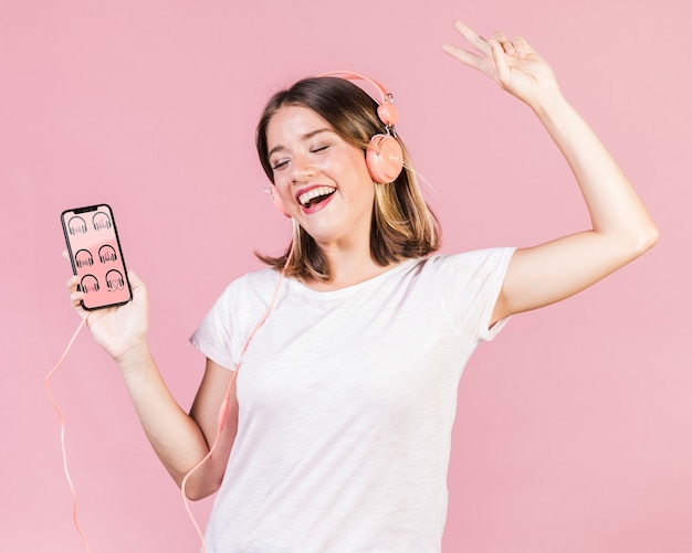 Giovane donna felice con le cuffie che tengono un modello del cellulare