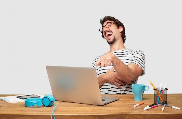 giovane graphic designer con la barba con un computer portatile che ride forte di qualcosa di esilarante