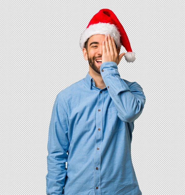 Giovane uomo che indossa cappello santa gridando felice e coprendo il viso con la mano