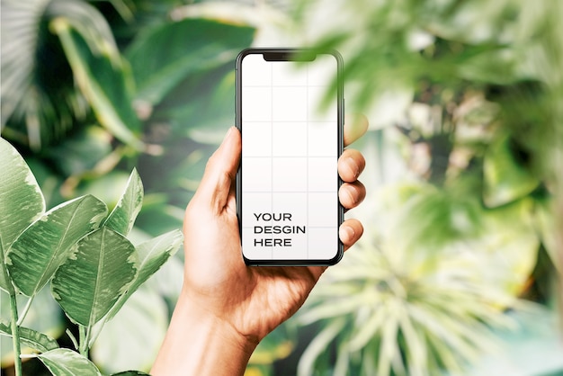 Hand hält neues Smartphone-Modell, umgeben von Blättern