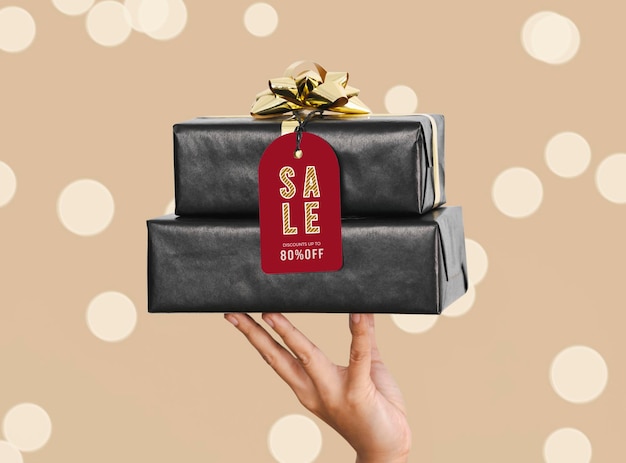 Hand mit schwarzer geschenkbox und mockup-weihnachtsgruß-tags auf weißem hintergrund