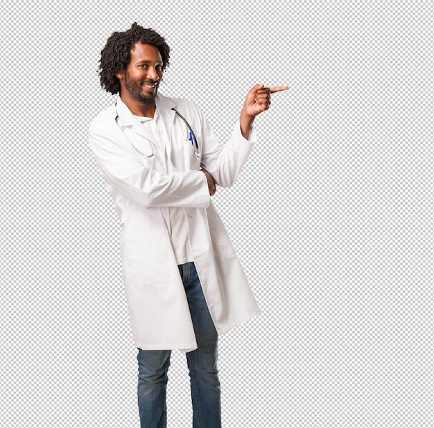 Hermoso médico afroamericano apuntando hacia un lado, sonriendo sorprendido presentando algo, natural y casual
