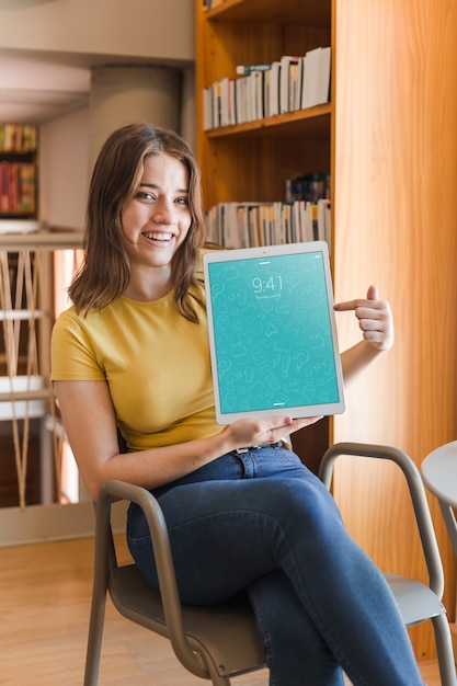 PSD heureuse femme tenant la maquette de la tablette dans la bibliothèque