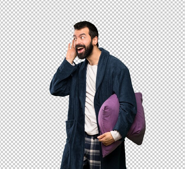 Hombre con barba en pijama escuchando algo poniendo la mano en la oreja