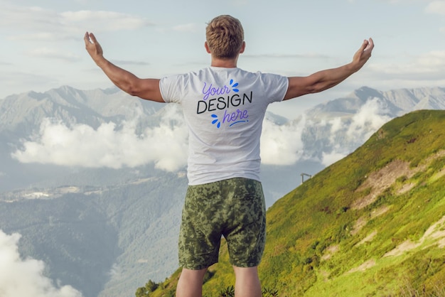 Hombre con los brazos levantados en una montaña con una camiseta blanca con un diseño disfrutando de la vista