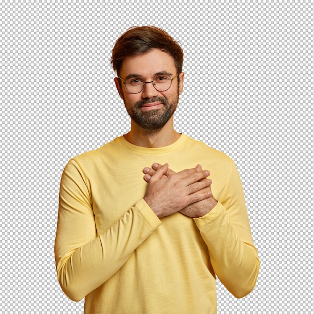 Hombre guapo con barba mantiene las manos en el corazón expresa emociones sinceras aprecia la ayuda y las palabras conmovedoras está agradecido usa un jumper amarillo casual posa en el interior concepto de lenguaje corporal