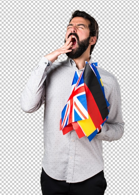 Hombre guapo con barba sosteniendo muchas banderas y bostezando
