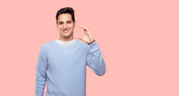 hombre guapo joven sonriendo con una expresión satisfecha que muestra un pequeño objeto o concepto