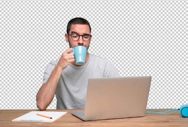 Hombre joven confidente que se sienta en su escritorio que bebe el café