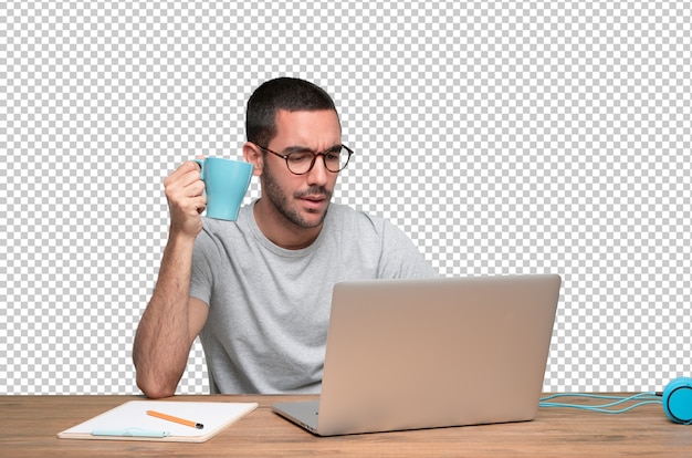 Hombre joven confidente que se sienta en su escritorio que bebe el café