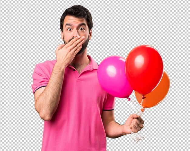 Hombre joven hermoso que sostiene los globos y que cubre su boca