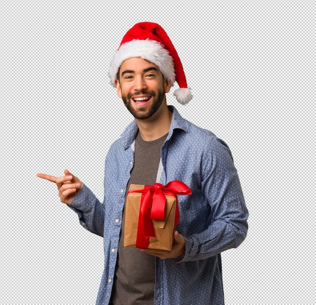 Hombre joven que lleva el sombrero de santa que señala al lado con el dedo