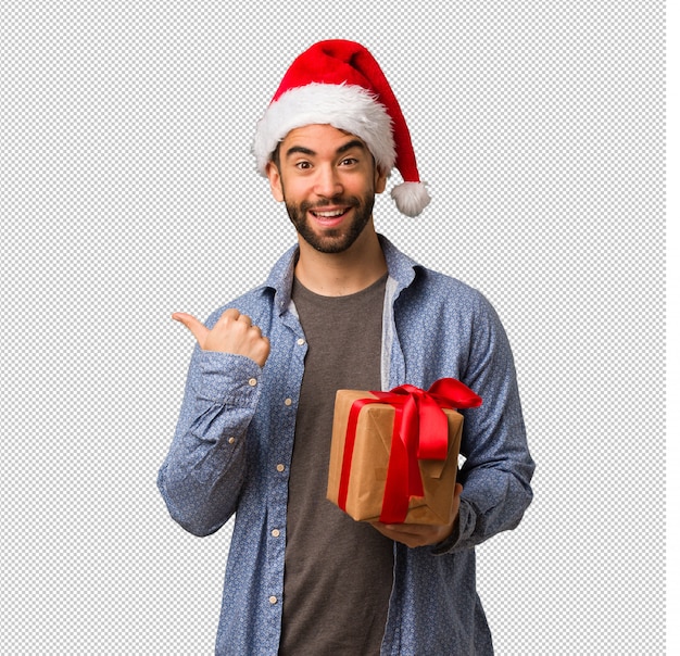 Hombre joven que lleva el sombrero de santa que señala al lado con el dedo