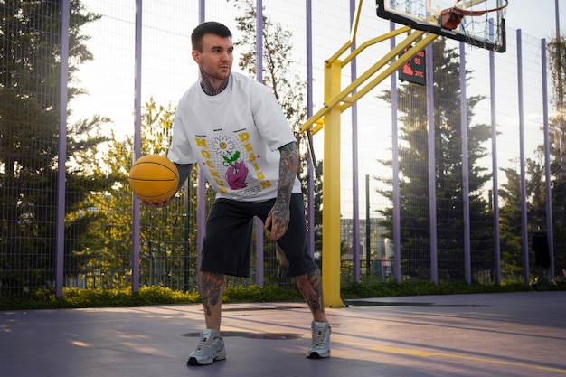 PSD homme portant une maquette de t-shirt cyber street wear avec un design urbain sur le terrain de basket