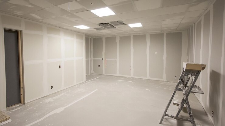 PSD interior da sala inacabada com instalação de parede de gesso em andamento mostrando escada de espaço vazio e iluminação encaixada