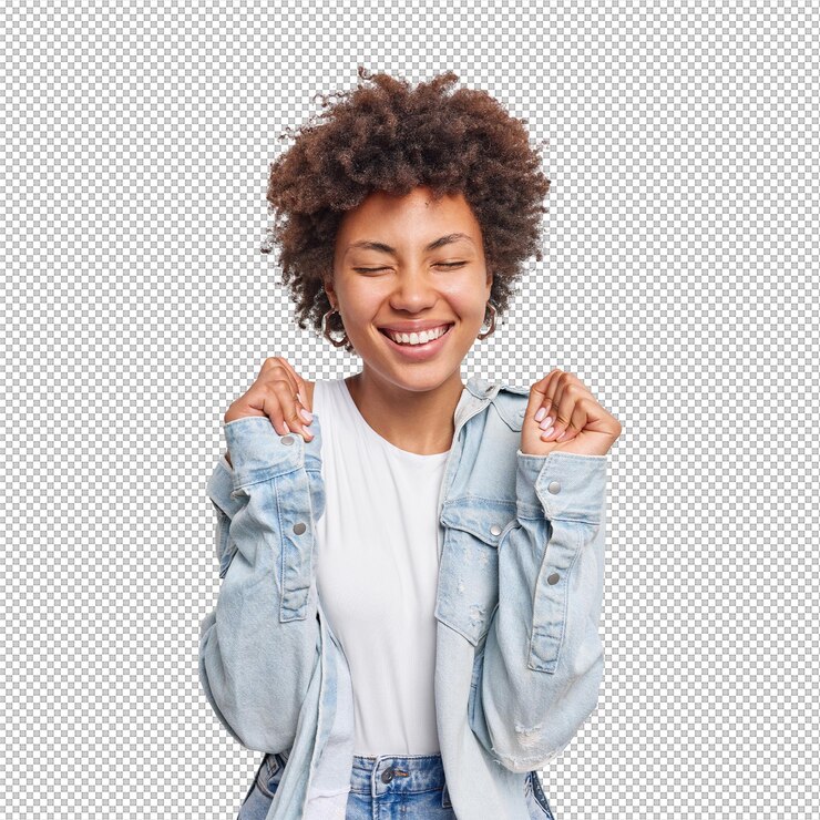 PSD une jeune femme aux cheveux bouclés positifs lève les mains attend les résultats se réjouit des nouvelles impressionnantes garde les yeux fermés sourit largement porte une chemise en jean isolée sur un mur blanc