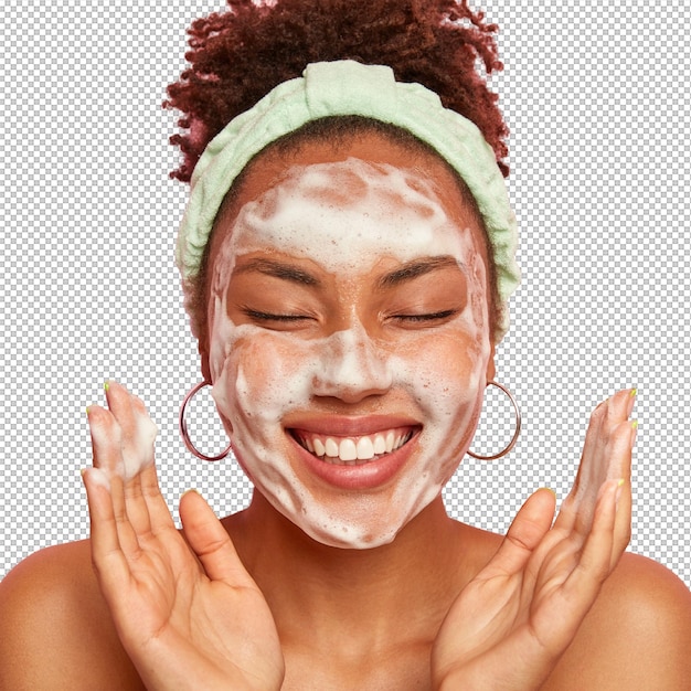 La jeune femme lève les paumes sur le visage garde les yeux fermés montre des dents blanches utilise de la mousse de nettoyage pour les soins de la peau obtient un vrai plaisir