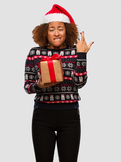 Jeune femme noire tenant un cadeau au jour de Noël, croise les doigts pour avoir de la chance