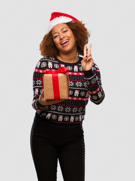 Jeune femme noire tenant un cadeau au jour de Noël faisant un geste de victoire