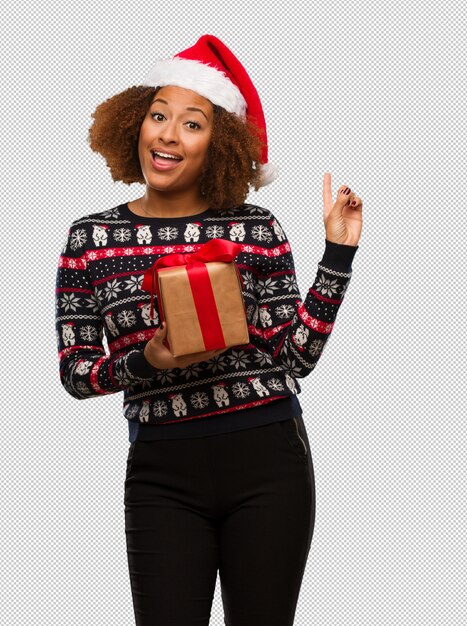 PSD jeune femme noire tenant un cadeau au jour de noël pointant vers le côté avec le doigt