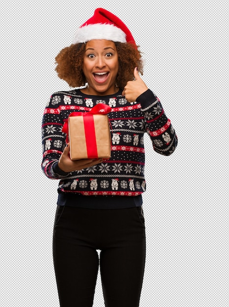 Jeune femme noire tenant un cadeau au jour de Noël surprise, réussie et prospère