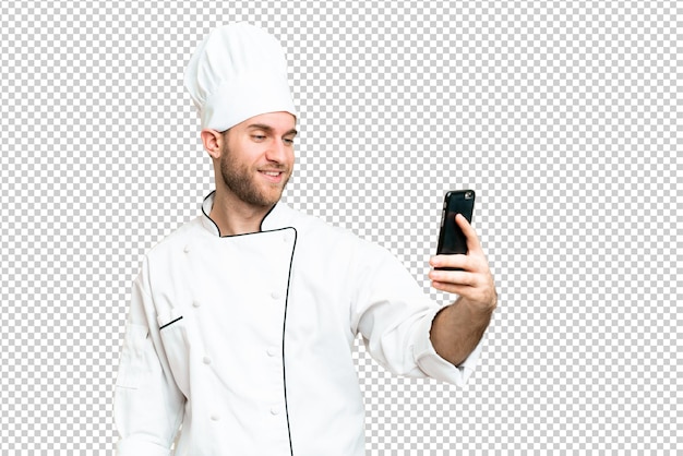 Un jeune homme blond, chef sur un fond de clé chrome isolé, fait un selfie.