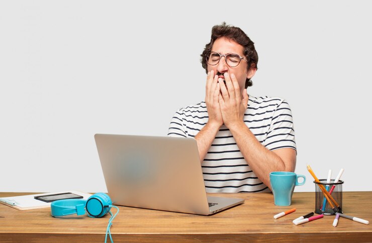 PSD jovem designer gráfico barbudo com um laptop procurando sem entusiasmo e entediado
