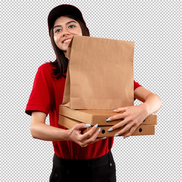 Jovem entregadora vestindo camisa polo vermelha e boné segurando pacote de papel e bolsas de pizza olhando de lado com um sorriso no rosto de pé sobre fundo rosa