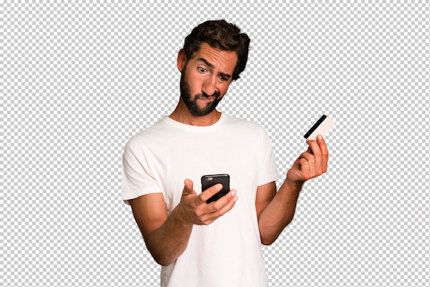 Jovem homem barbudo e expressivo fazendo compras on-line com telefone e cartão de crédito