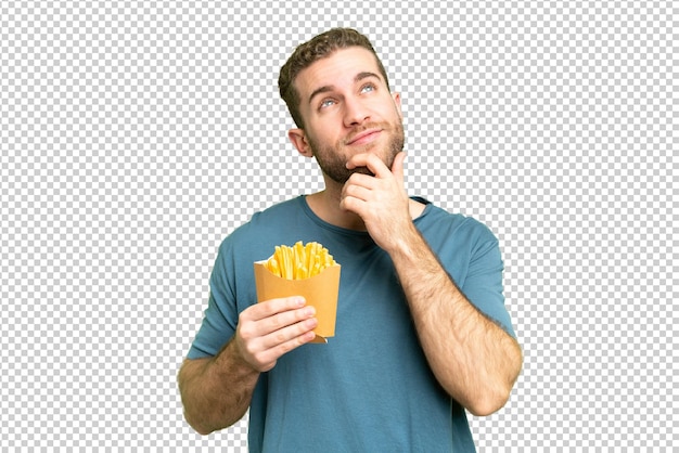 Jovem homem loiro bonito segurando batatas fritas sobre fundo de chave de croma isolado e olhando para cima